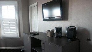 A hotel room with a flat-screen TV mounted on the wall, a coffee maker, and a cabinet.