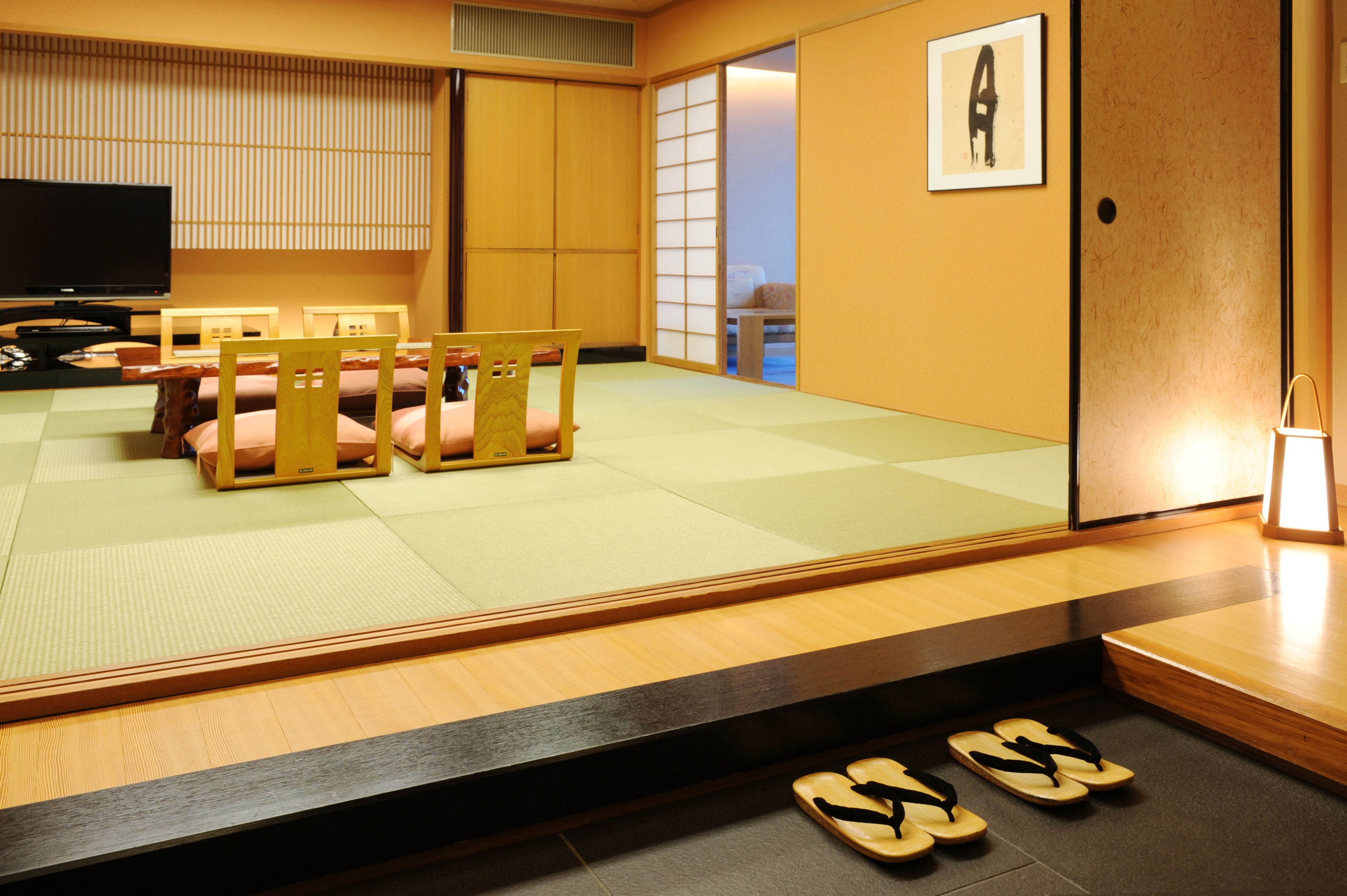 A traditional Japanese room with tatami flooring, a television, and a sliding door leading to a balcony.