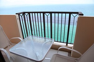 Un balcón con una mesa de vidrio y dos sillas, con vista al mar turquesa.