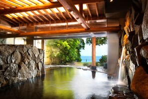 A spa area with a stone wall, wooden beams, and a view of the ocean. - AoAwo Naruto Resort (Naruto)