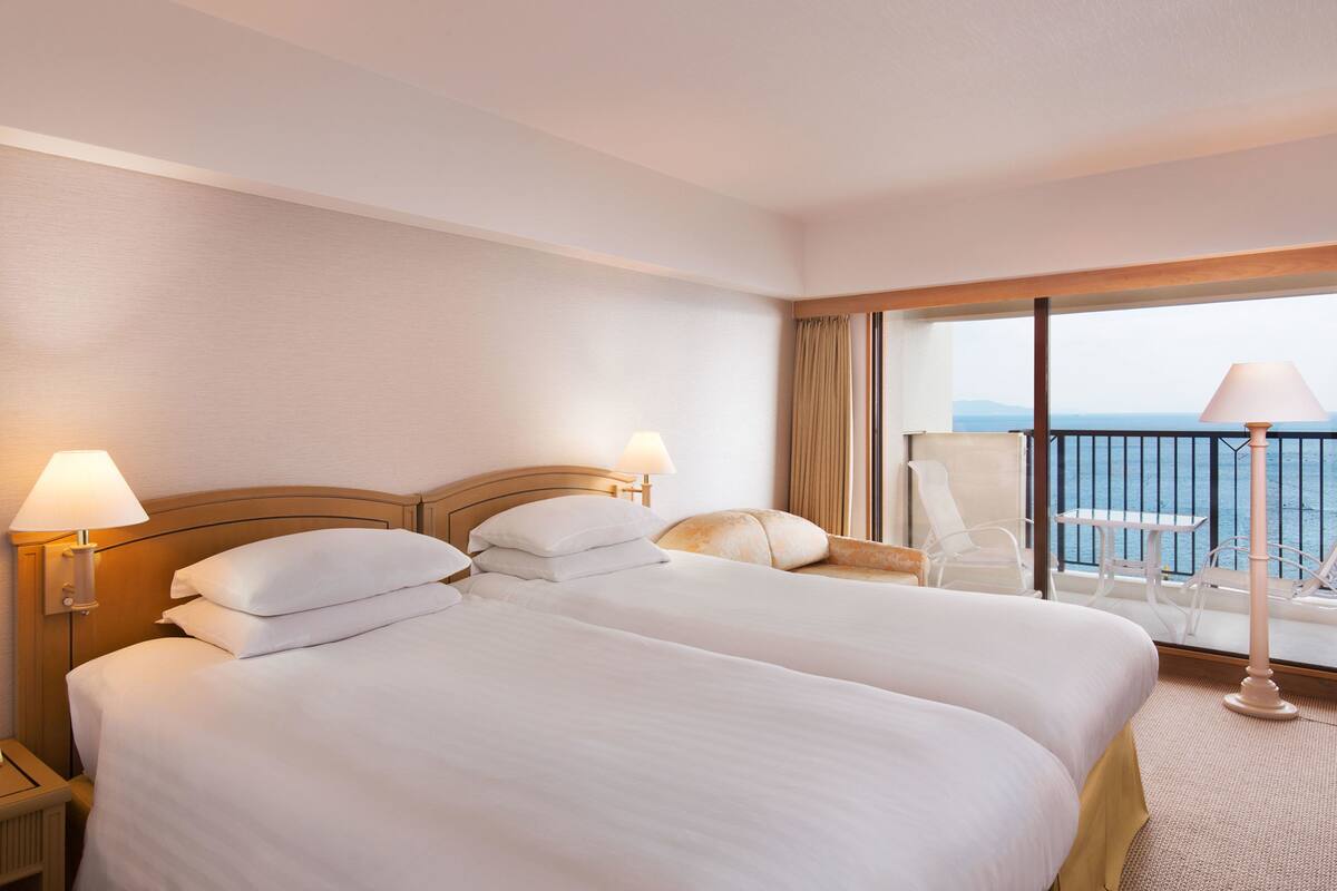 A hotel room with two beds, a balcony with a table and chairs, and a view of the sea.