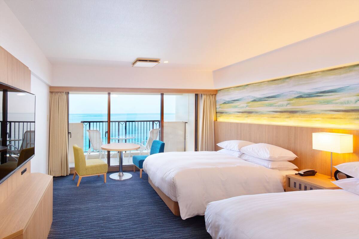 A hotel room with a balcony, a TV, a desk, and a painting.