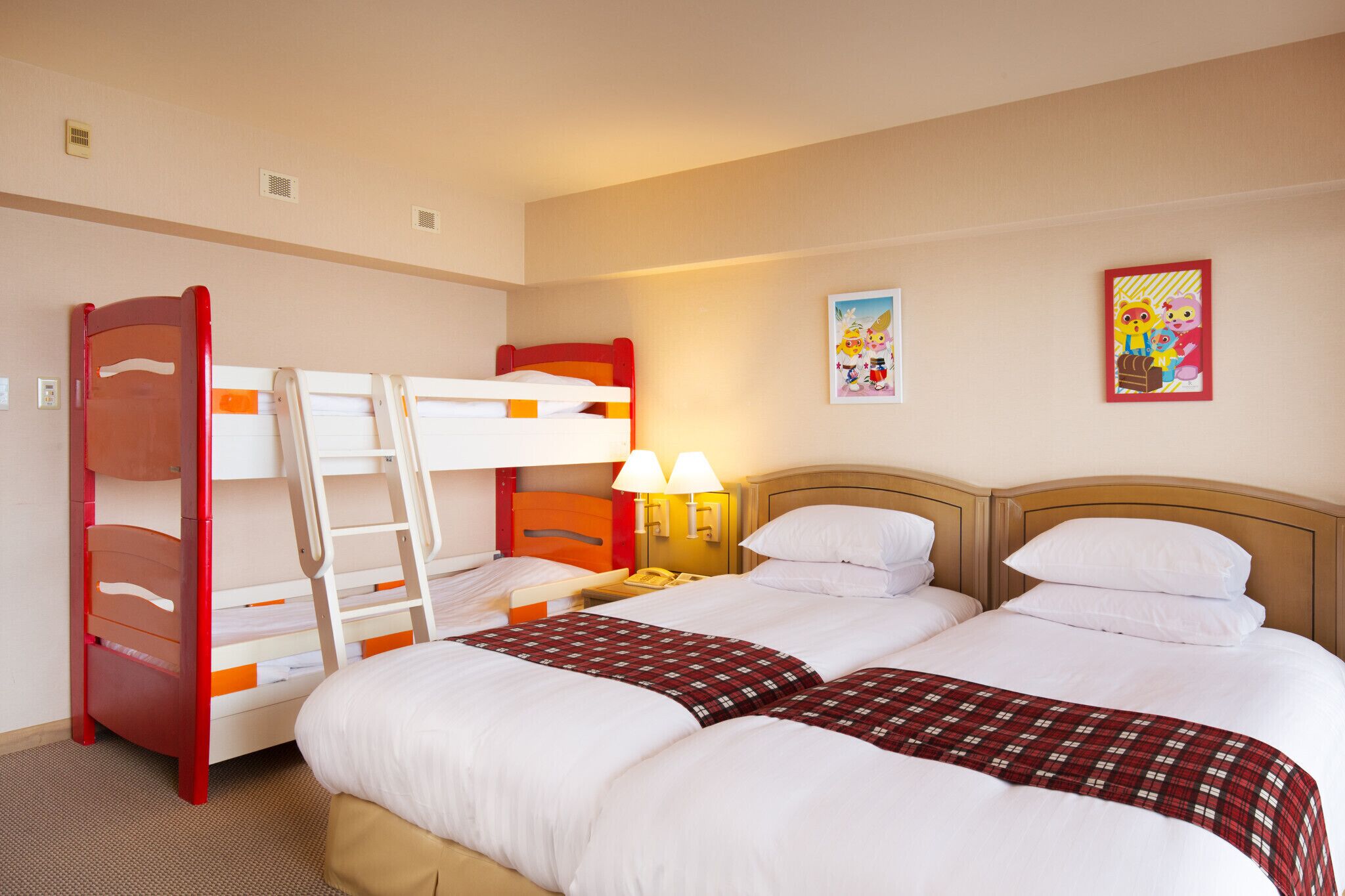 A hotel room with bunk beds, a bedside table with a lamp, and two wall art pieces.