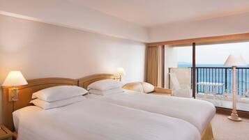 A hotel room with two beds, a balcony with a view of the sea, and a table and chair set up for dining.