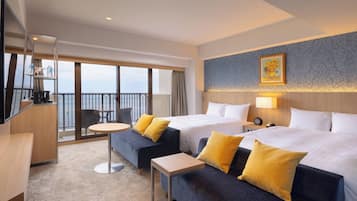 Habitación de hotel con dos camas, un sofá, una mesita, televisor y balcón con vistas.