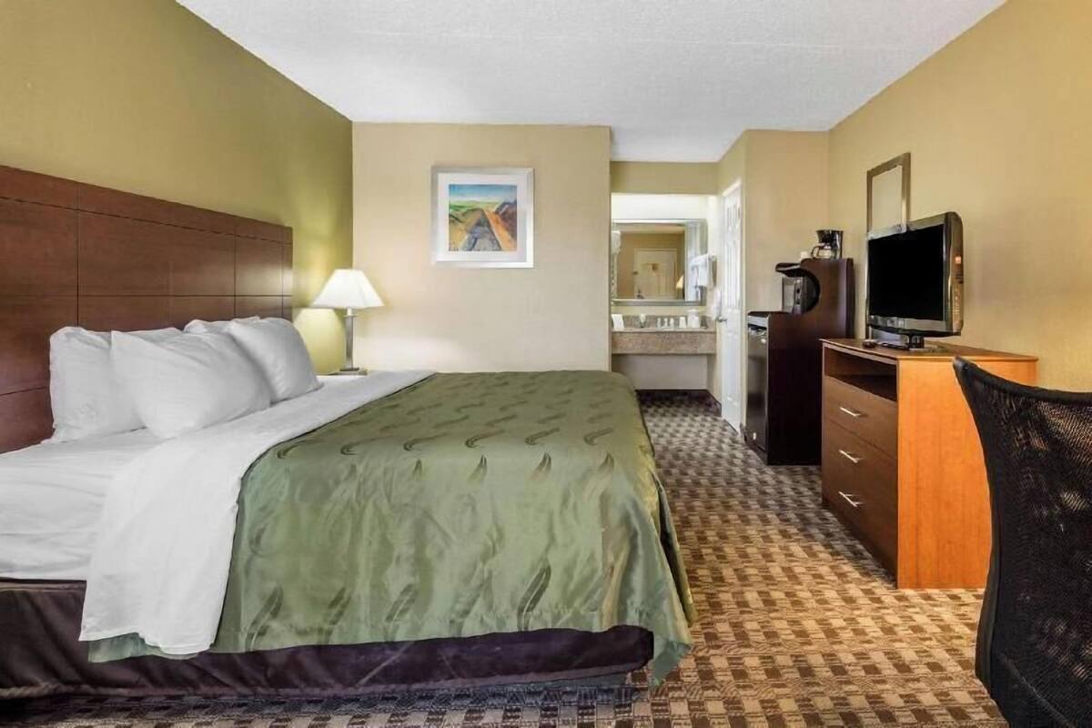 A hotel room with a bed, a desk, a television, and a bathroom visible through an open door.