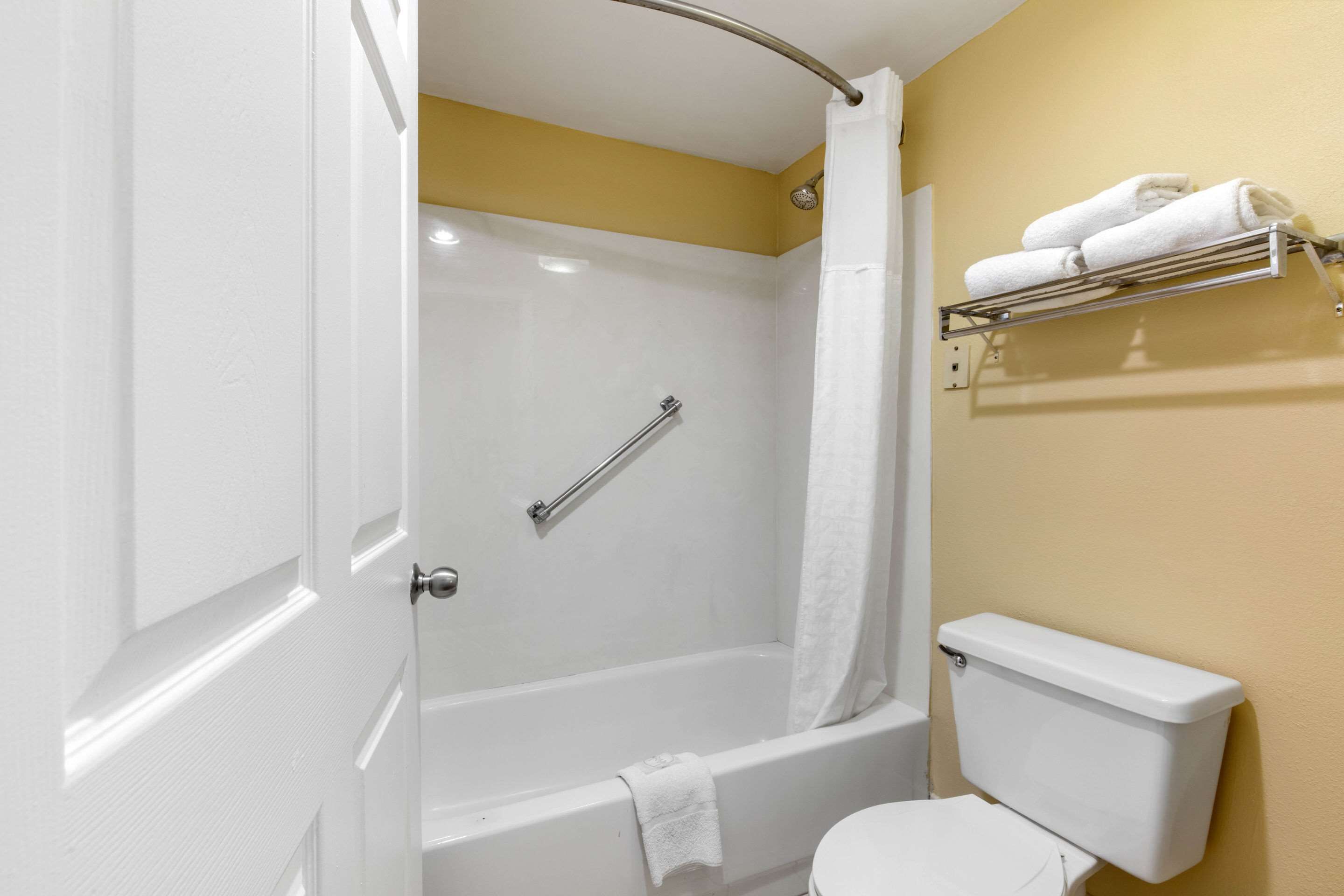 A bathroom with a white bathtub, a white toilet, and a towel rack with towels.