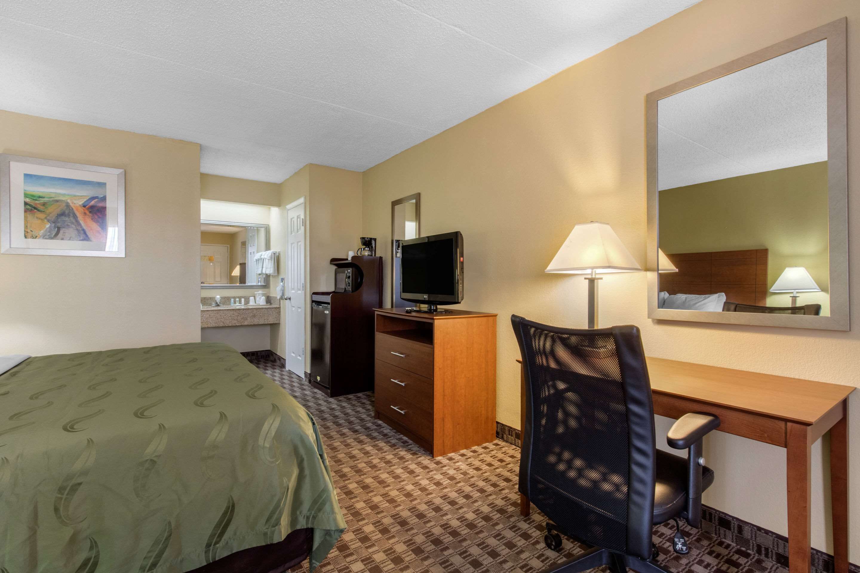 A hotel room with a bed, desk, chair, TV, and a mirror.