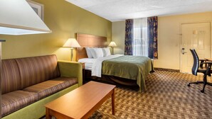 A hotel room with a bed, a green sofa, a wooden table, and a desk with a chair. - Quality Inn Lebanon (Lebanon)