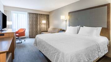 A hotel room with a large bed, a desk with a TV, a chair, and a window with curtains.