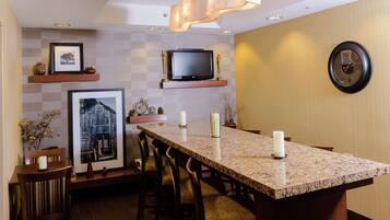 A modern kitchen with a granite countertop, wooden chairs, a television above the counter, and a wall clock.