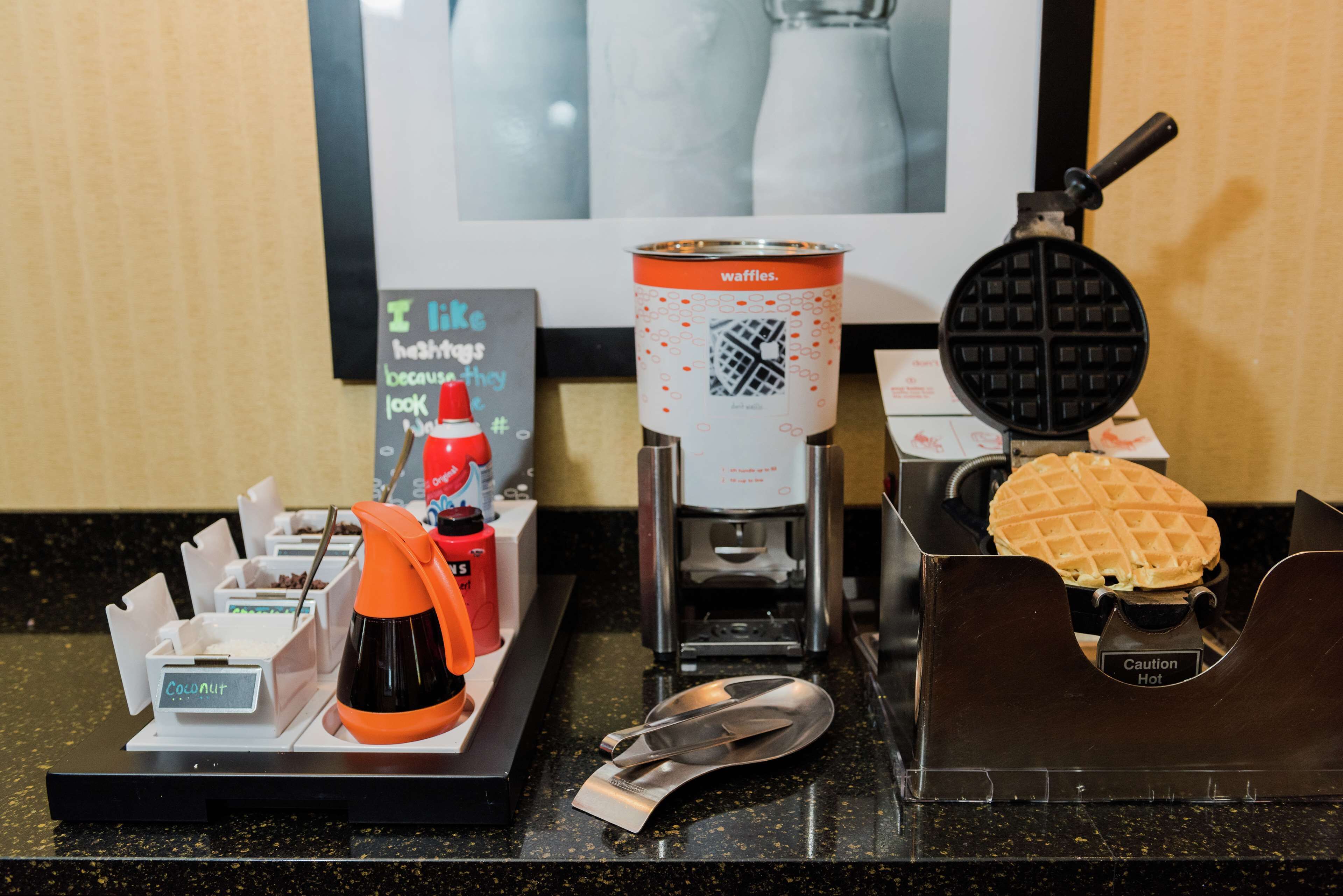 A waffle maker, a waffle, and a coffee machine on a countertop.