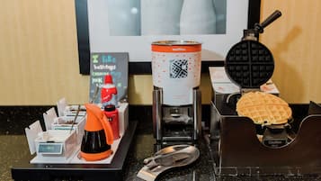 Una máquina para hacer gofres, un gofre y una cafetera sobre una encimera.