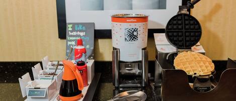 Una máquina para hacer gofres, un gofre y una cafetera sobre una encimera.