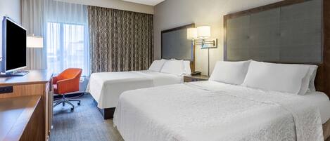 Quarto de hotel com duas camas, uma escrivaninha, televisão e uma cadeira.