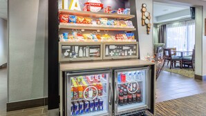 Vestíbulo de hotel con una mesa de snacks, un área de descanso y dos refrigeradores para bebidas.