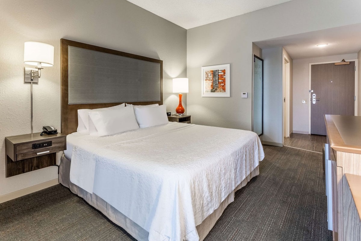 Une chambre d’hôtel avec un grand lit, des lampes de chevet, une table de chevet, un bureau et une porte donnant sur une autre pièce.