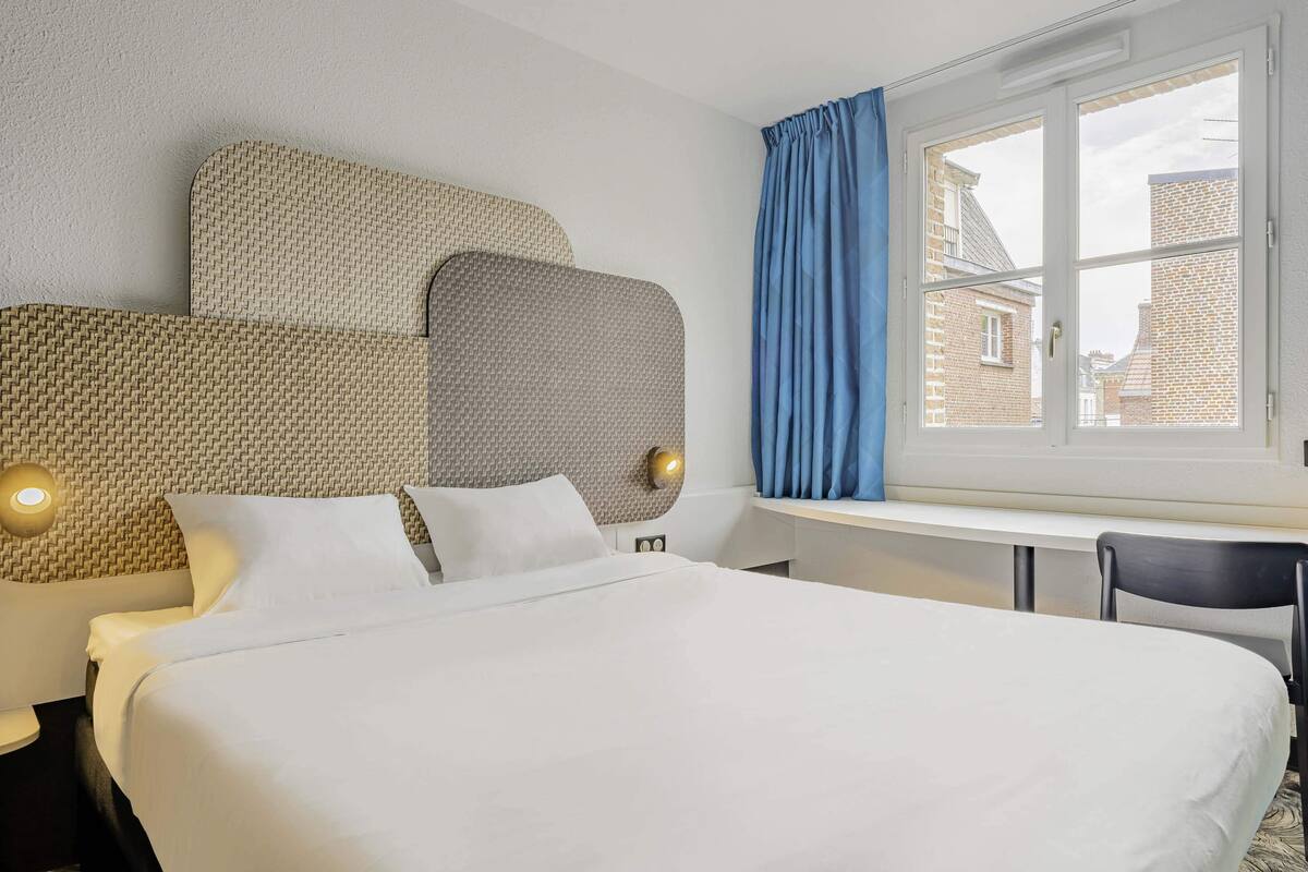 Una habitación de hotel con una cama grande, un escritorio y una ventana con cortinas.
