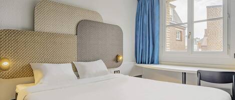 A hotel room with a large bed, a desk, and a window with curtains.