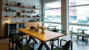 A cafe with a wooden table, chairs, shelves with items, and large windows. - Max Brown Hotel 5th District, part of Sircle Collection (Vienna)