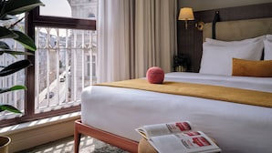 A hotel room with a large bed, a window with a view of buildings, a lamp, and a magazine on the bed. - Max Brown Hotel 5th District, part of Sircle Collection (Vienna)