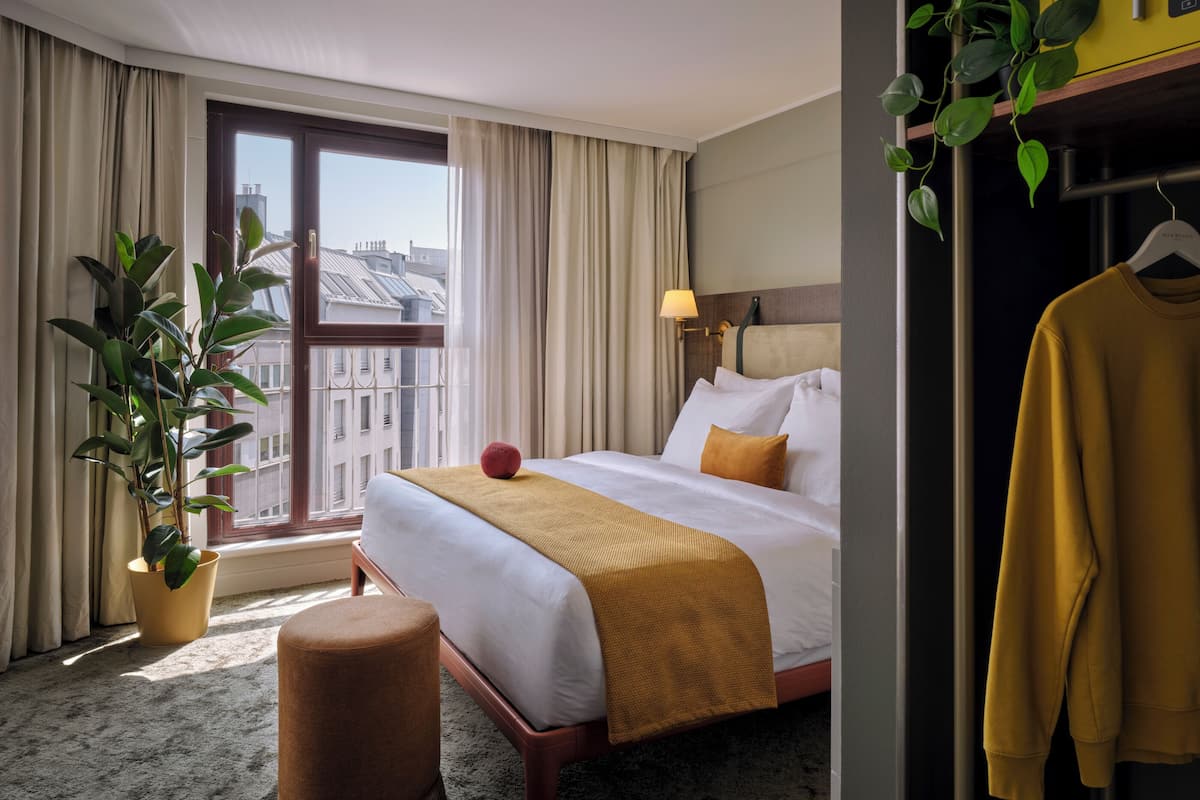 Une chambre d’hôtel avec un lit, une plante en pot, une plante suspendue, une lampe et une armoire.