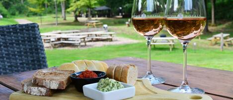 A wooden table with a cutting board holding sliced bread, a small bowl of spread, and two glasses of wine.