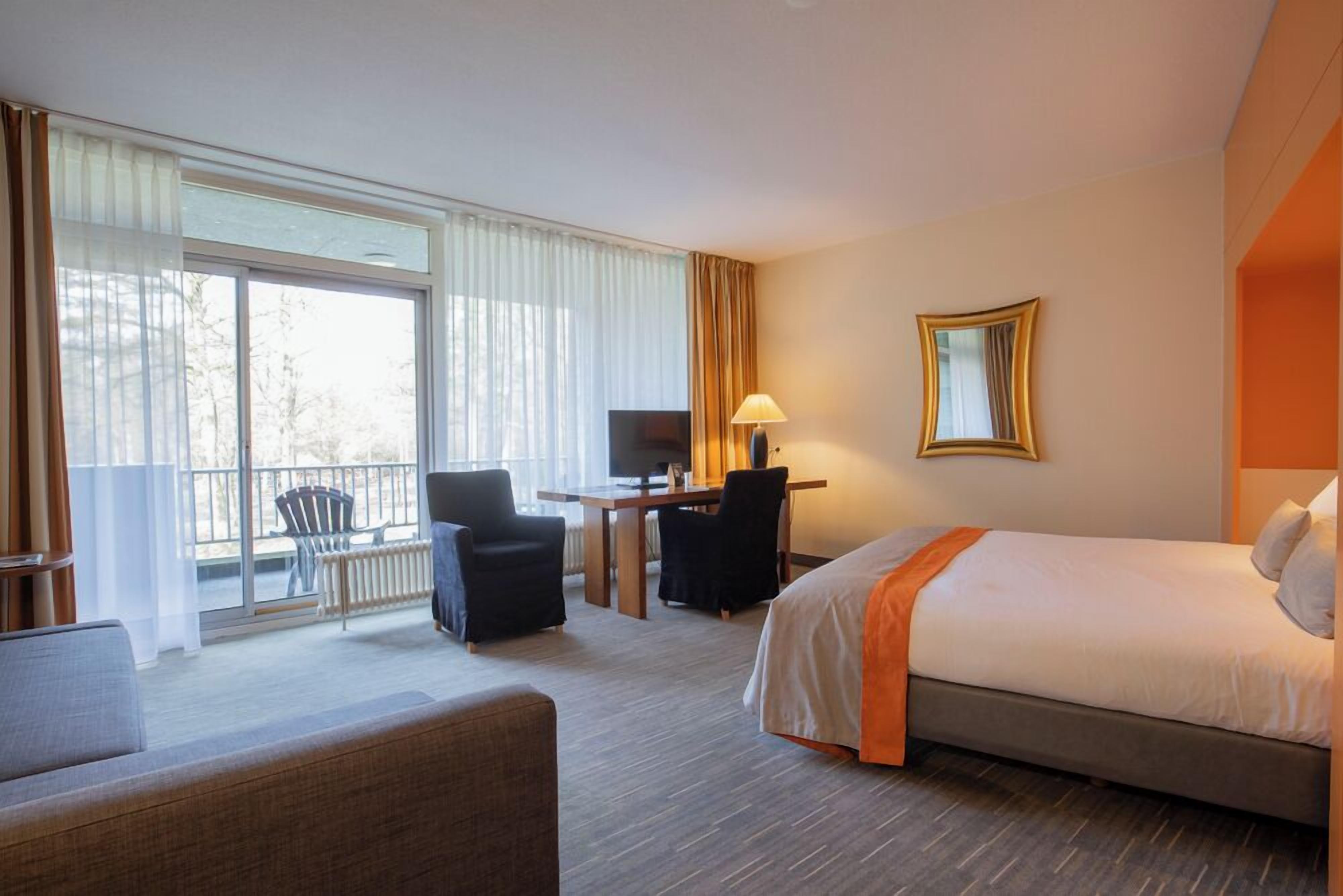 A hotel room with a bed, a desk, a chair, a TV, and a balcony with a chair.