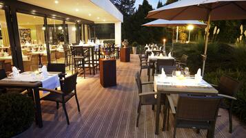 Een terras met tafels en stoelen, met een modern gebouw op de achtergrond en een goed verlicht terras.