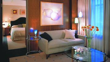 Une chambre d’hôtel avec un canapé, une table basse en verre, un vase avec des fleurs et un tableau au mur.