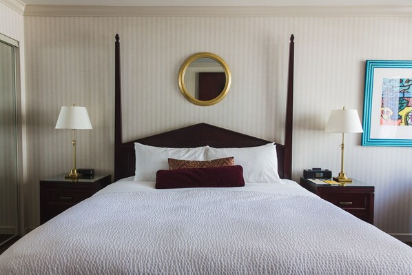 A neatly made bed with a white duvet, two bedside tables with lamps, a large mirror, and a framed picture on the wall.