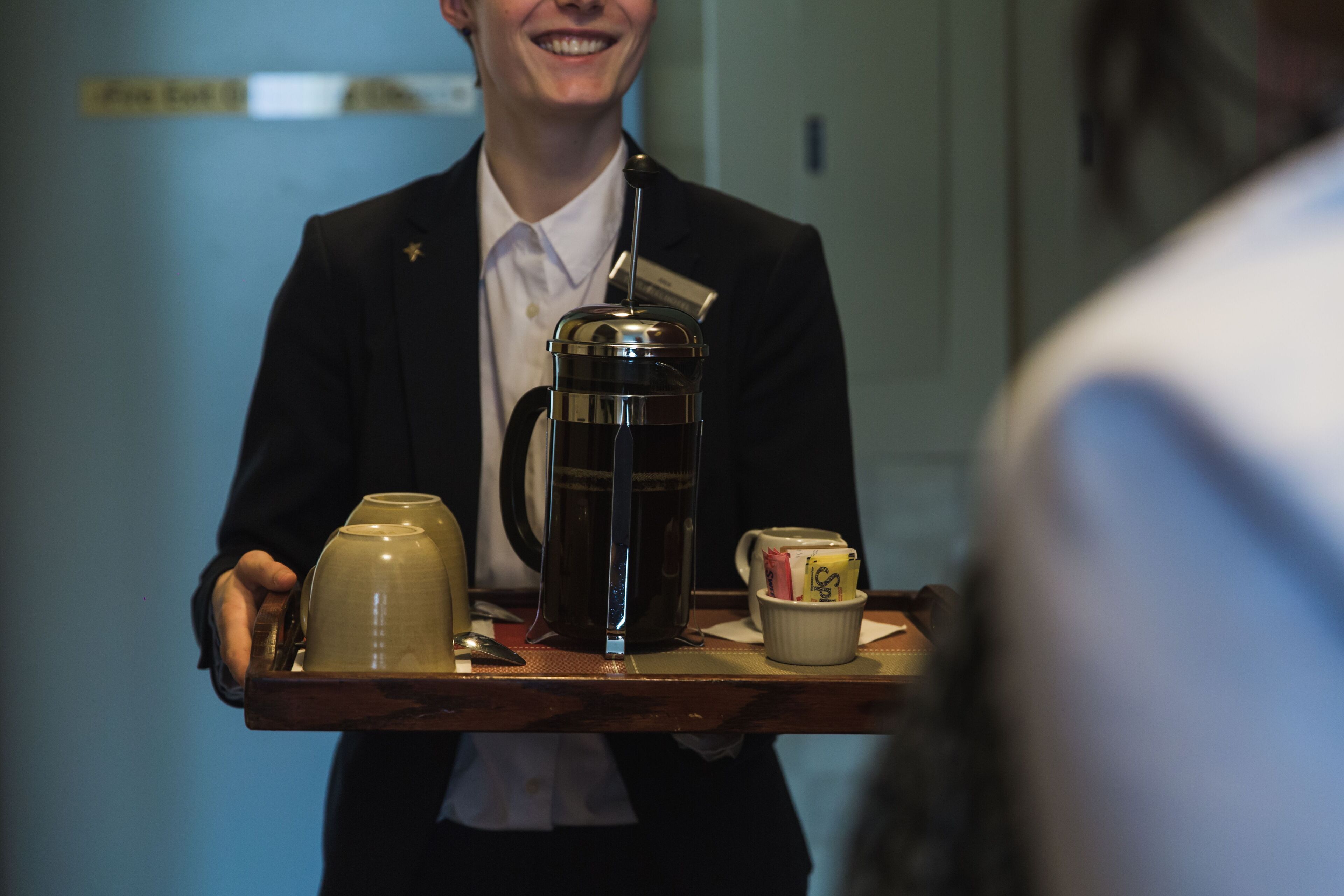 A person holding a tray with a coffee pot, a mug, and a teapot.
