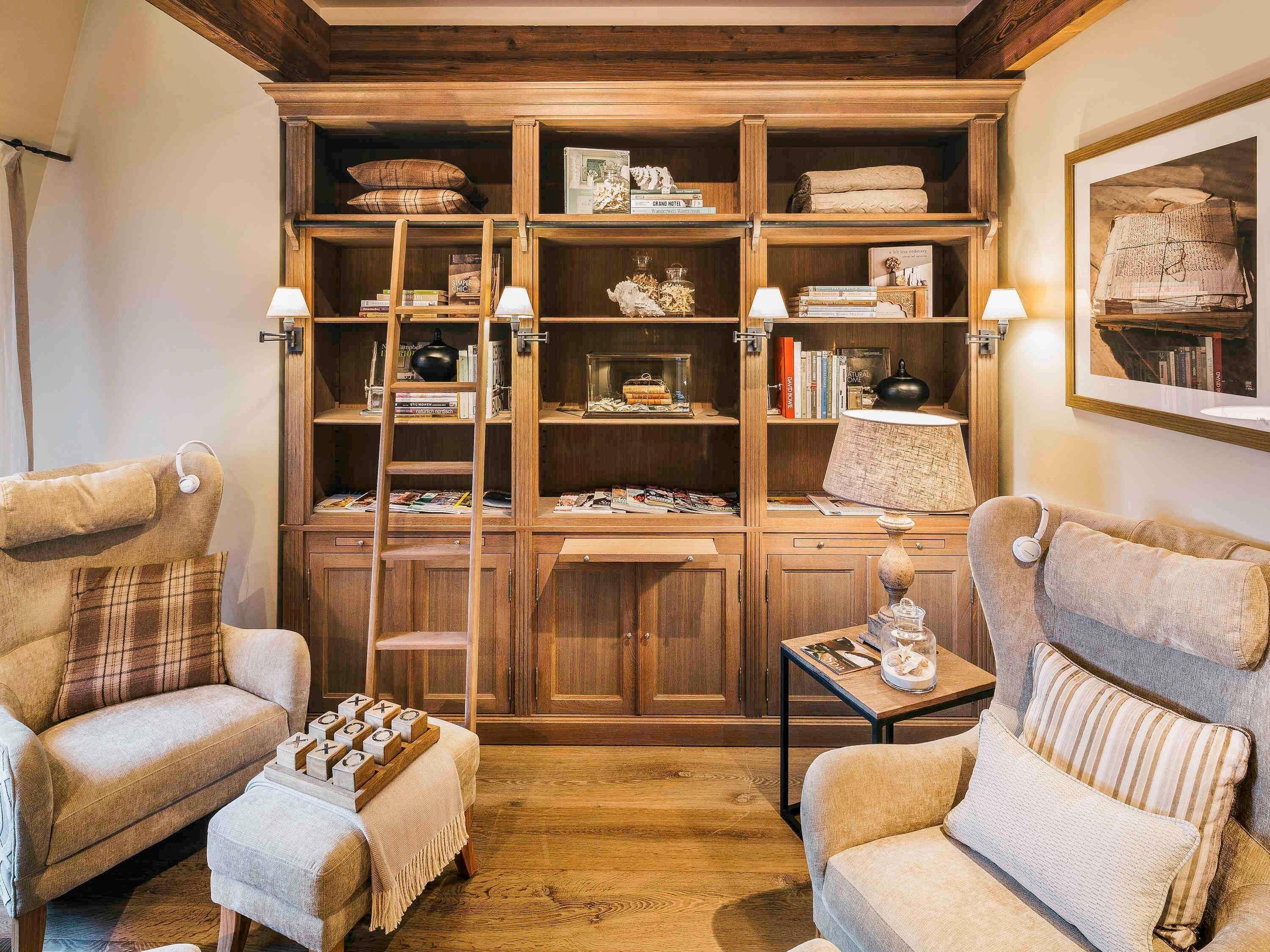A cozy room with wooden shelving, two armchairs, a small table, and a lamp.