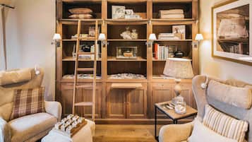A cozy room with wooden shelving, two armchairs, a small table, and a lamp.