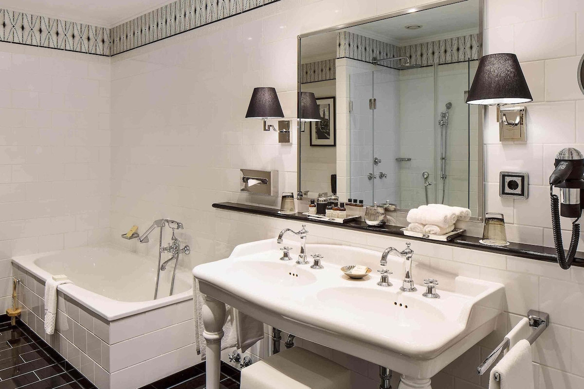 A bathroom with a bathtub, two sinks, a large mirror, and a hairdryer.