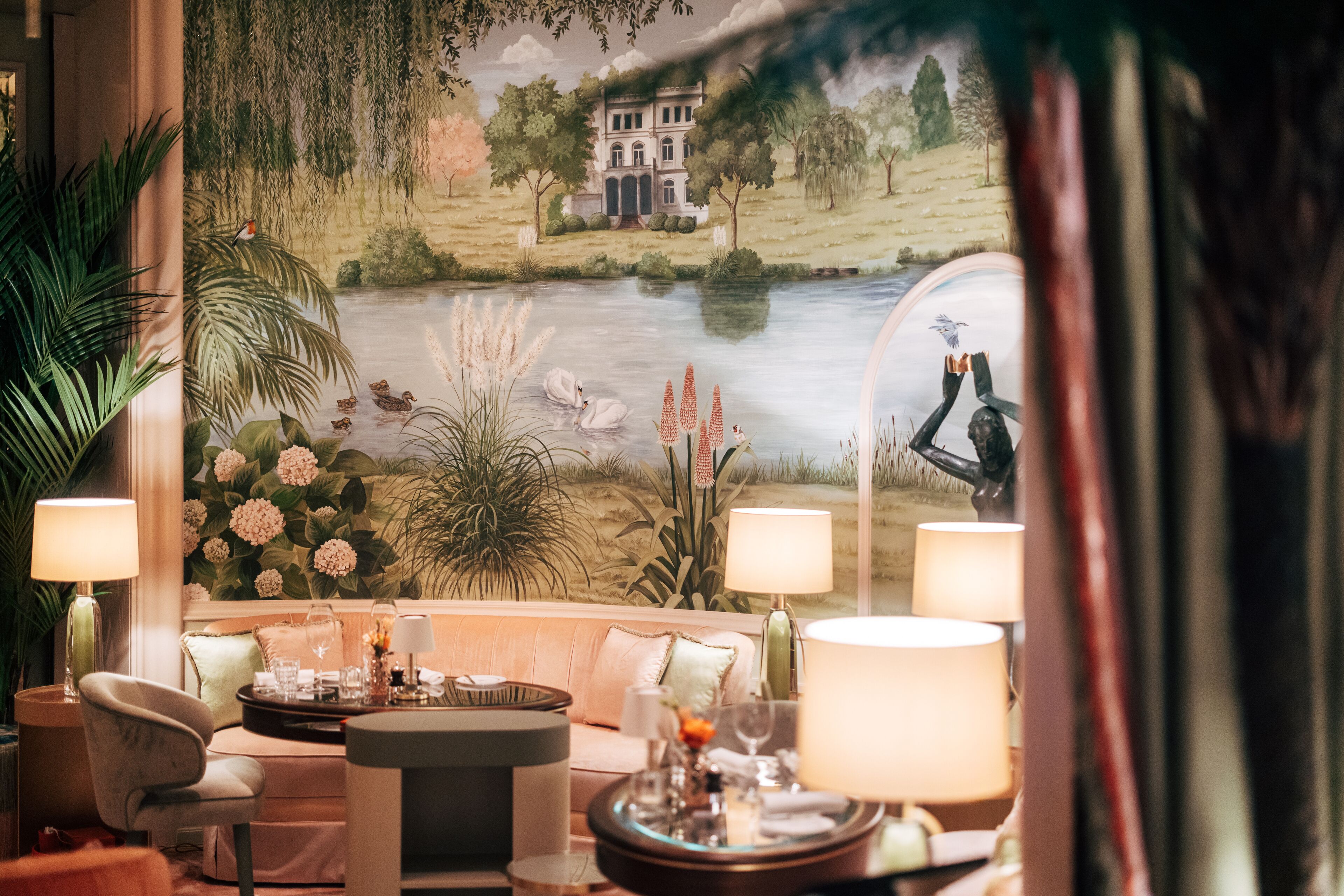A room with a large window, a sofa, a table with a lamp, and a decorative mirror.