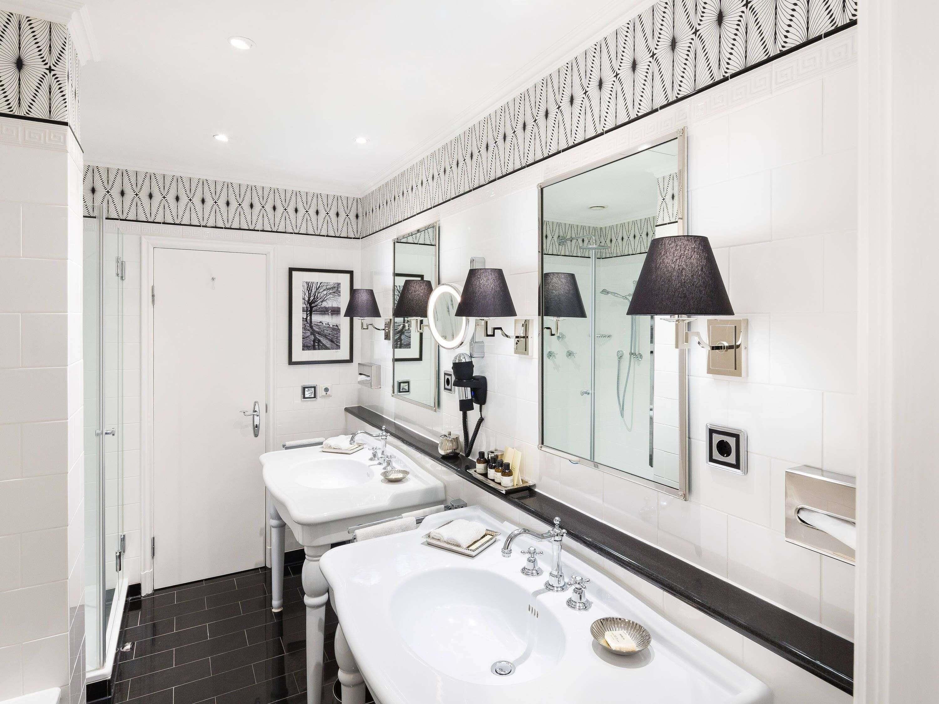Een moderne badkamer met twee wasbakken, grote spiegels en zwarte lampen.
