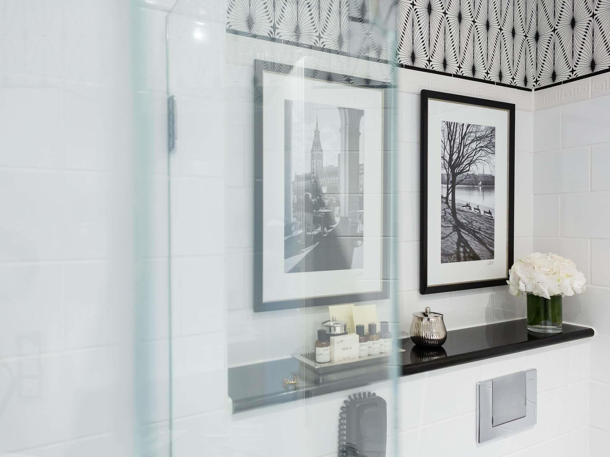 A bathroom with a glass shower enclosure, a black countertop with a vase of white flowers, and two framed black and white photographs on the wall.