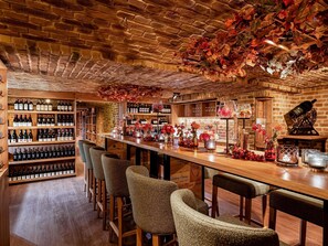 A bar area with wooden shelves of wine bottles, a long bar counter, and bar stools.