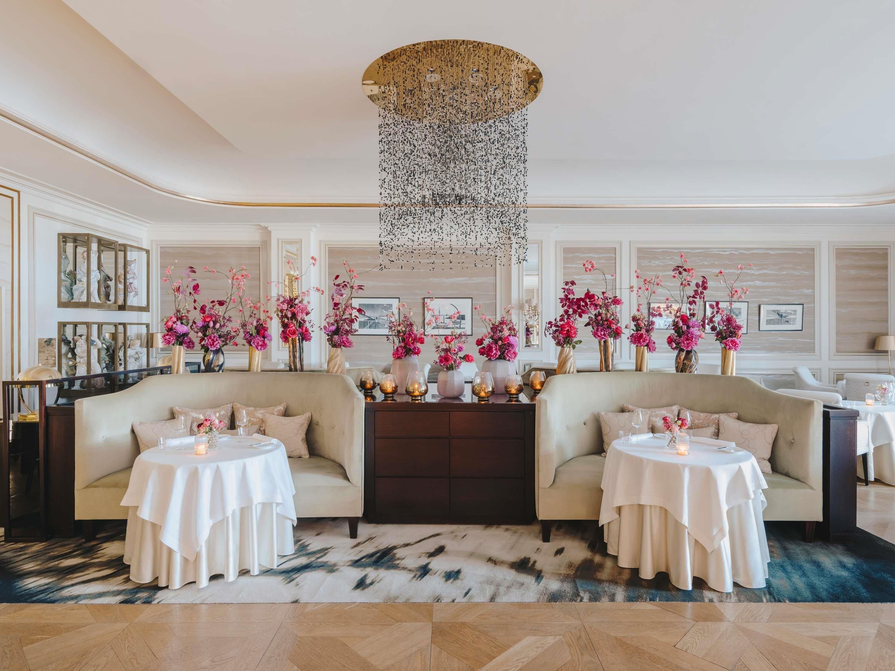 A luxurious hotel lobby with two sofas, round tables, and floral arrangements.