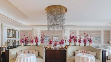 A luxurious hotel lobby with two sofas, round tables, and floral arrangements.