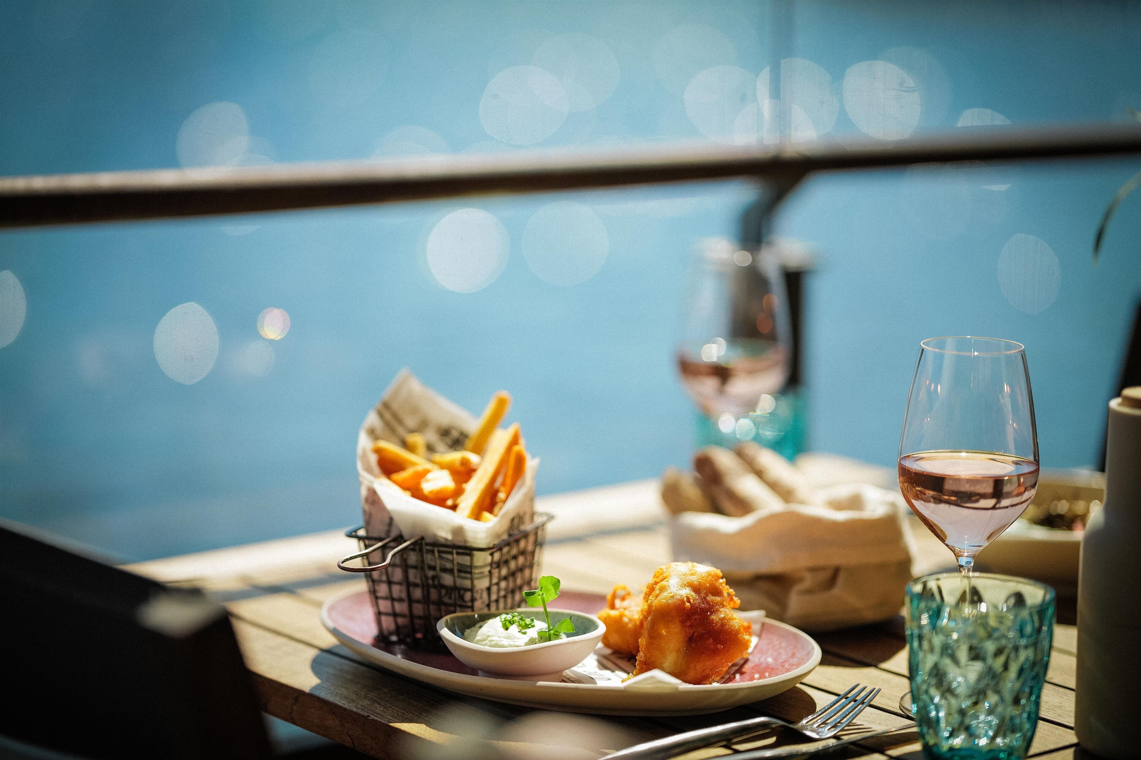 A table with a plate of food, a glass of wine, and a small bowl of sauce.
