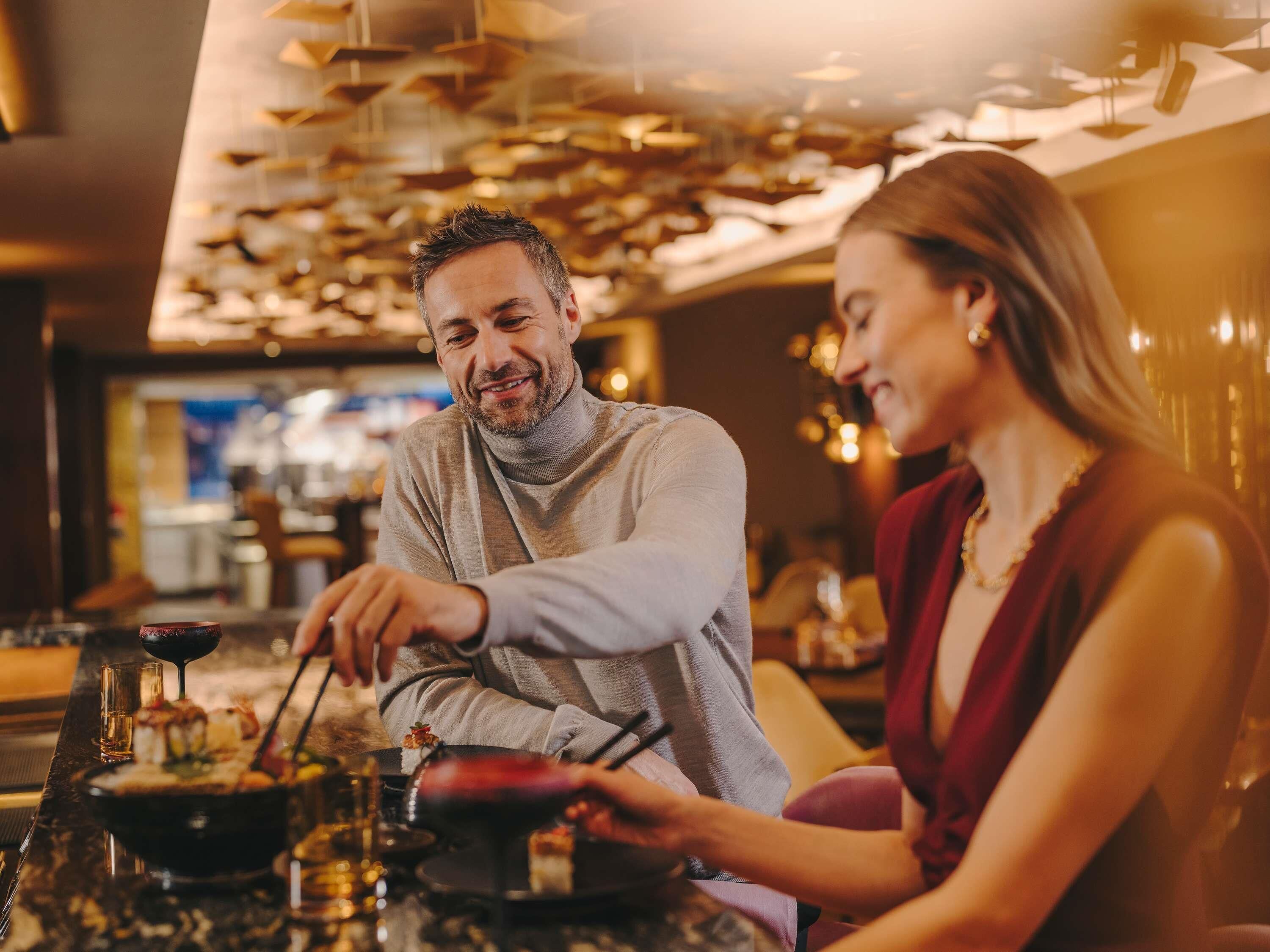 A couple dining at a restaurant with a modern interior and a visible bar area.