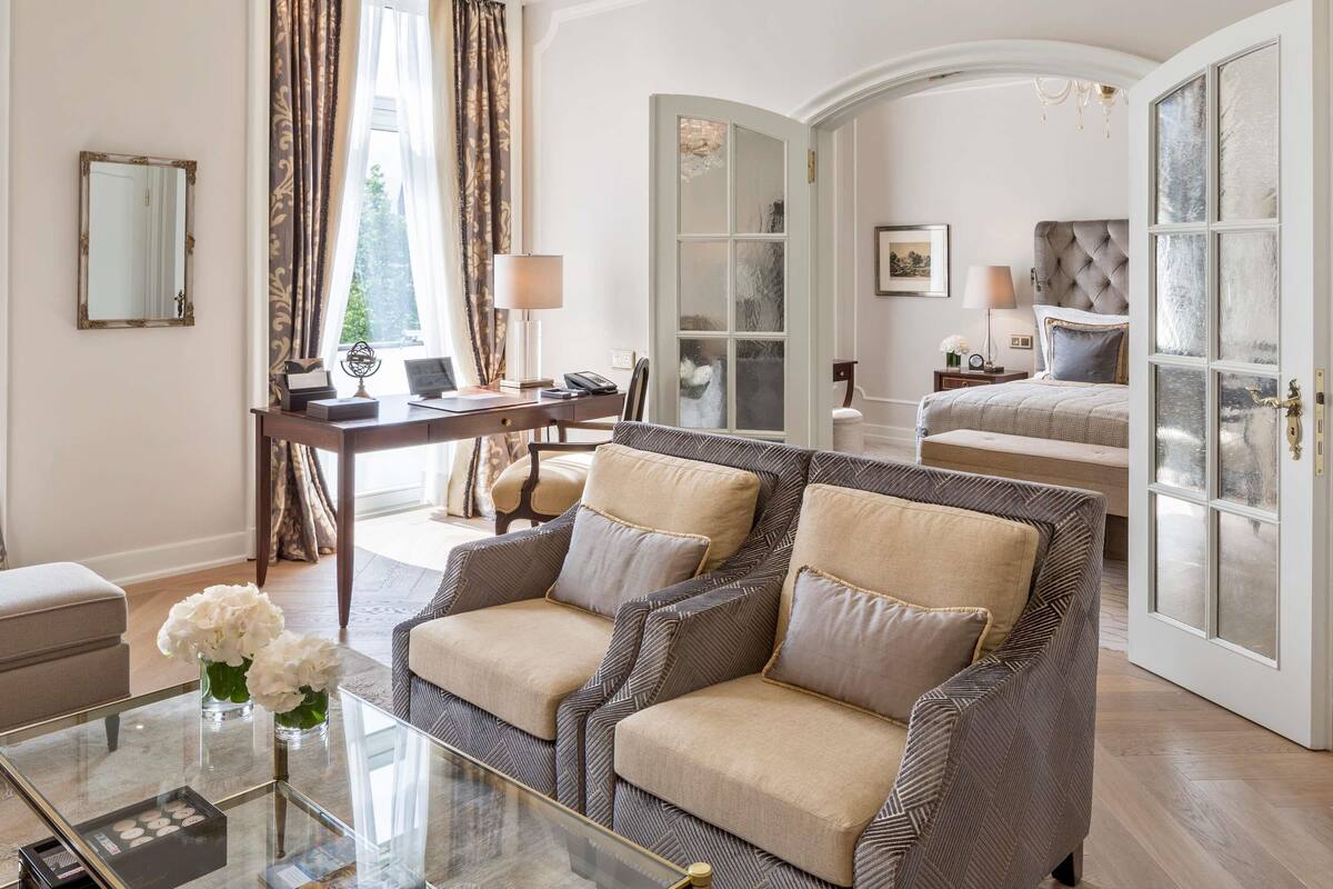 A hotel room with a sofa, a desk, a bed, and a glass door.