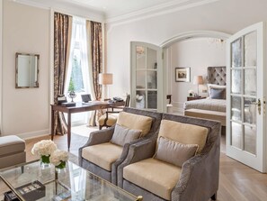 A hotel room with a sofa, a desk, a bed, and a glass door. - Fairmont Hotel Vier Jahreszeiten Hamburg (Hamburg)