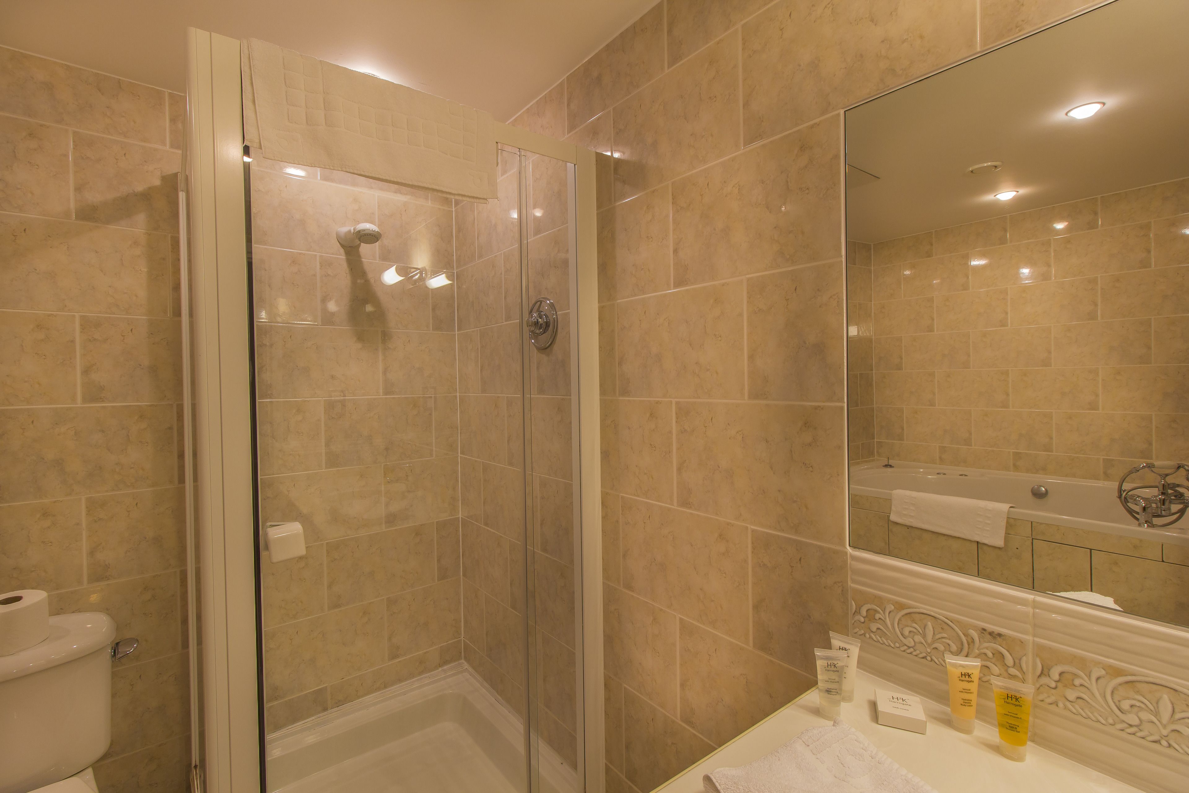 A bathroom with beige tiles, a glass-enclosed shower, a toilet, and a vanity with toiletries.