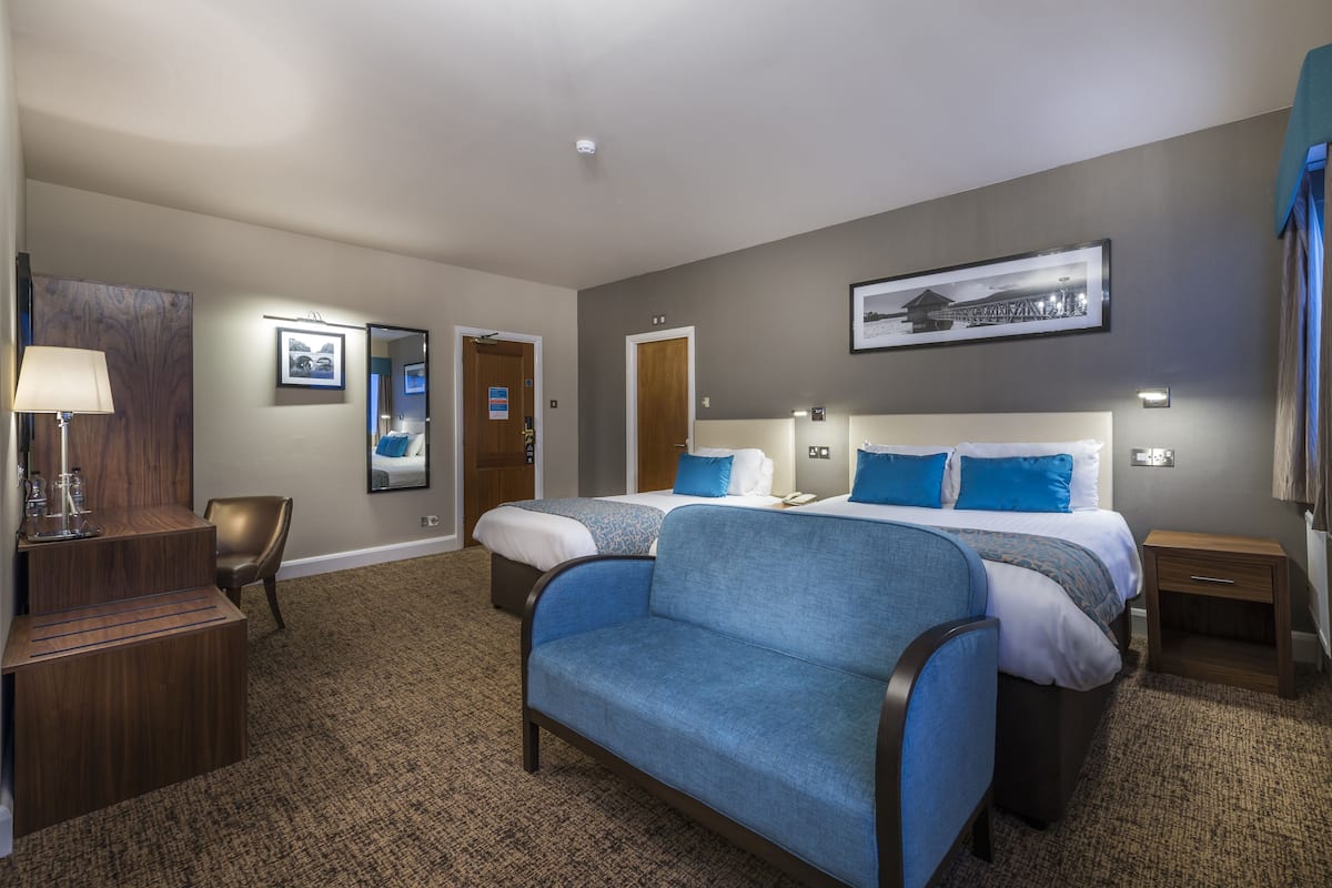 A hotel room with two beds, a sofa, a desk, and a mirror.