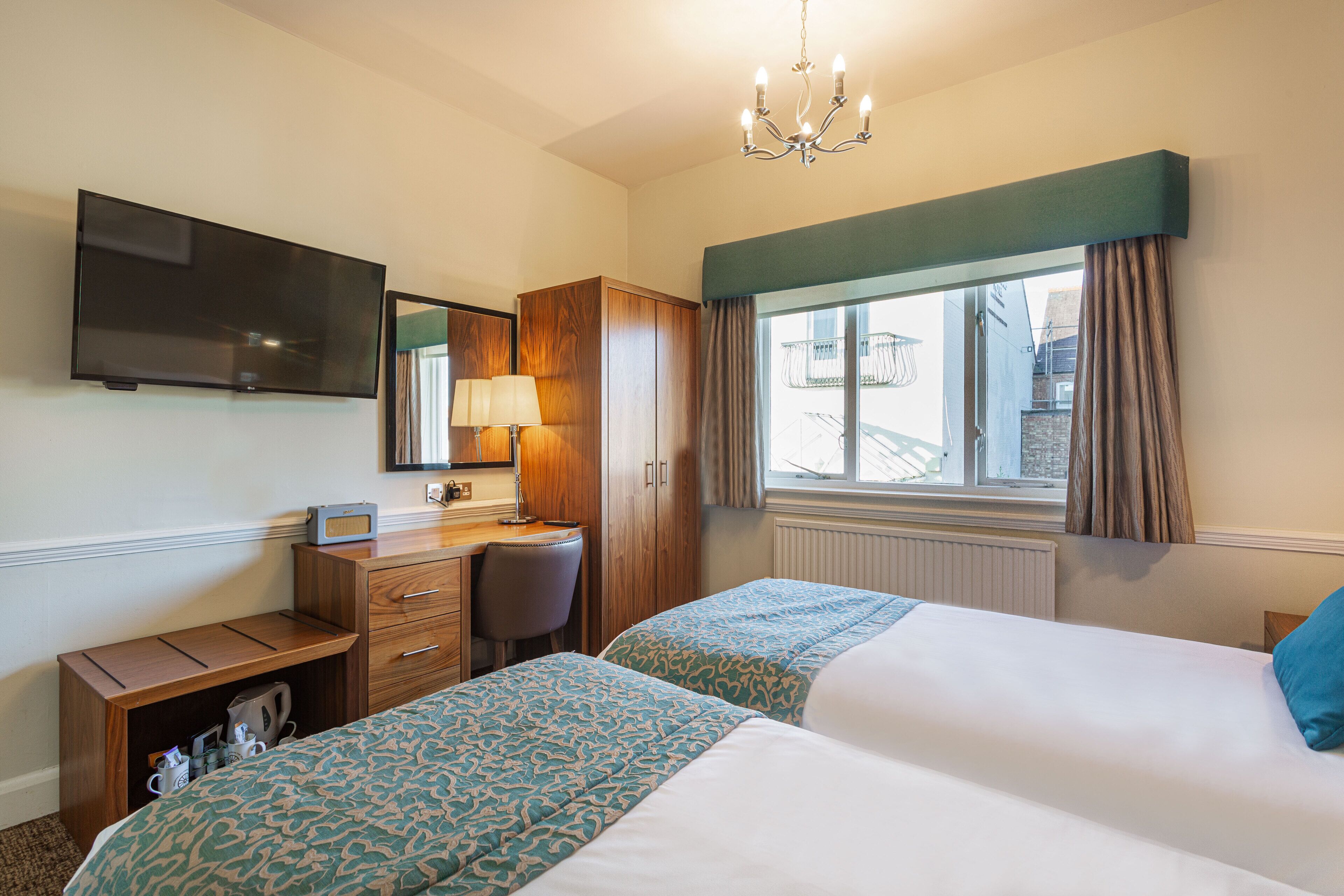 A hotel room with two beds, a desk, a chair, a television, and a window with curtains.