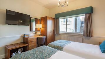 A hotel room with two beds, a desk, a chair, a television, and a window with curtains.