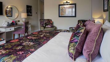 A hotel room with a large bed, a desk, two chairs, a round mirror, and framed pictures on the walls.
